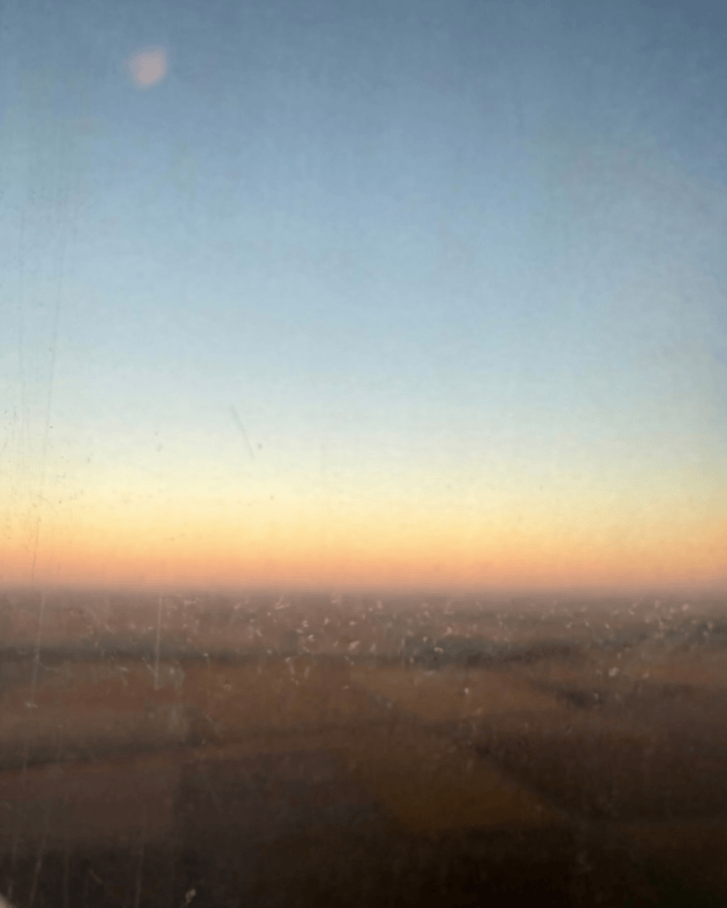 sunset view through plane window. blue at the top, goes into ombre orange at the middle. brown land at the bottom. 